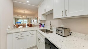 A modern kitchen with white cabinetry, a granite countertop, a stainless steel toaster, and a double sink. - Anna Maria Island Beach Palms 2A (Bradenton Beach)