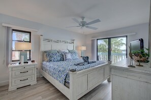 A bedroom with a bed, bedside tables, a ceiling fan, and a view of the outdoors. - Anna Maria Island Beach Palms 2B (Bradenton Beach)
