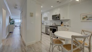 A modern kitchen with white cabinetry, a microwave, and a dining area with white chairs. - Anna Maria Island Beach Palms 2B (Bradenton Beach)