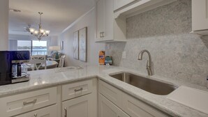 A modern kitchen with white cabinetry, a granite countertop, and a stainless steel sink. - Anna Maria Island Beach Palms 2B (Bradenton Beach)