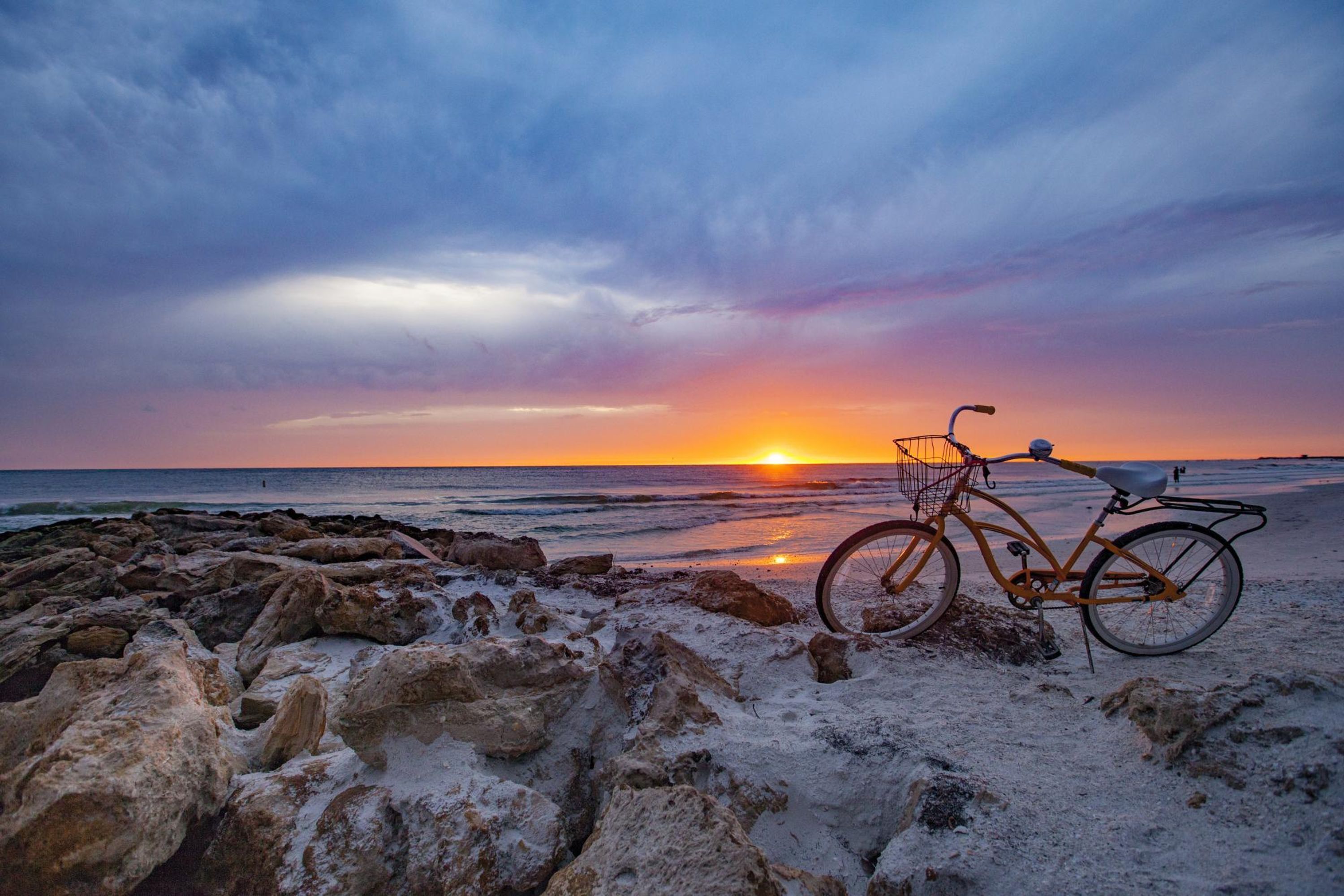 Una bicicleta estacionada en una playa rocosa al atardecer.