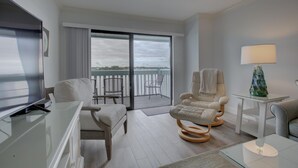 A modern hotel room with a balcony, a sofa, a chair, a table, and a lamp. - Anna Maria Island Beach Palms 2B (Bradenton Beach)
