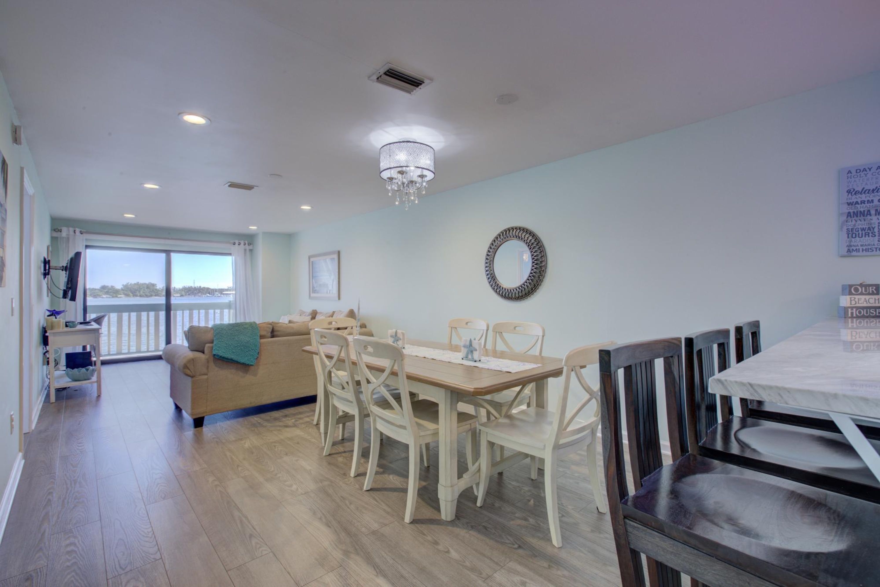 A dining area with a wooden table and chairs, a chandelier, and a view of the outdoors through large windows.