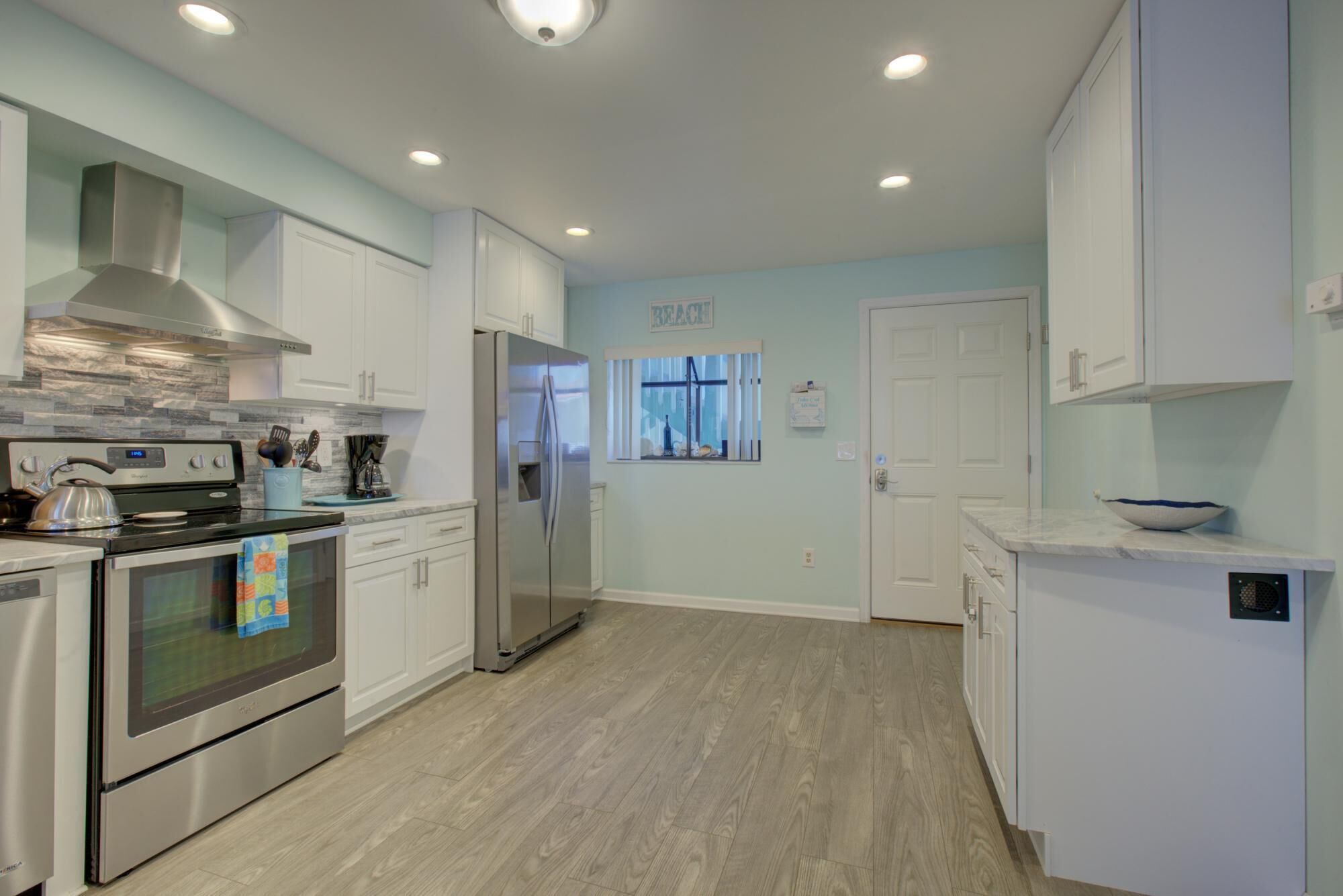 A modern kitchen with white cabinets, stainless steel appliances, and a wooden floor.