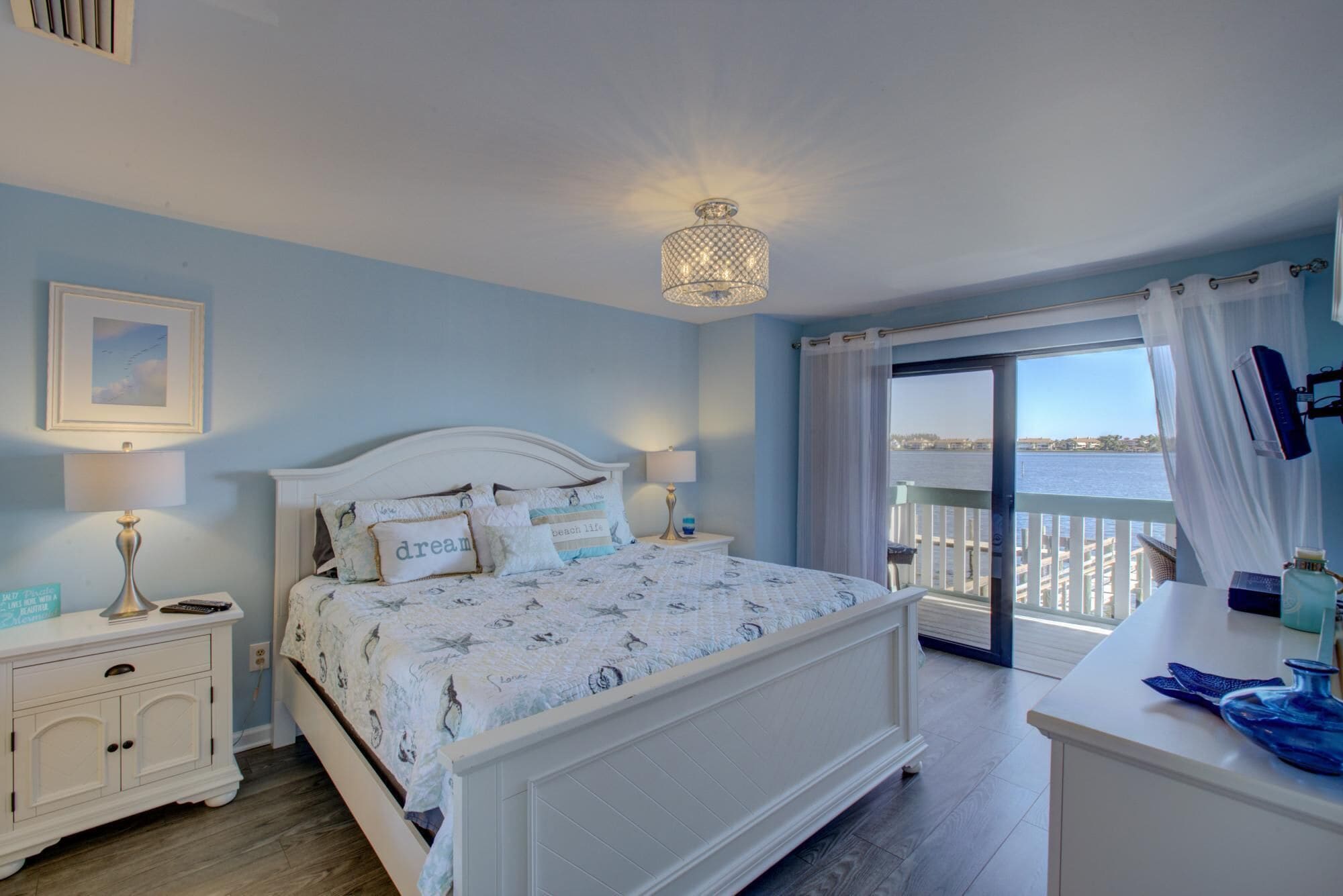 A bedroom with a bed, bedside tables, a lamp, a picture on the wall, and a view of the sea through a window.