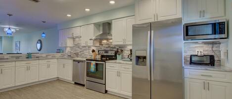 A modern kitchen with white cabinets, stainless steel appliances, and a wood floor.
