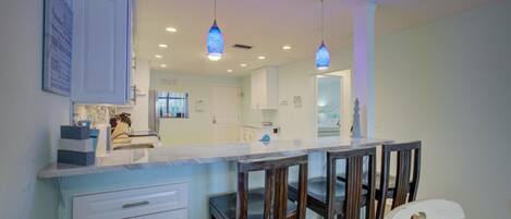 A modern kitchen with a central island, bar stools, and pendant lighting.