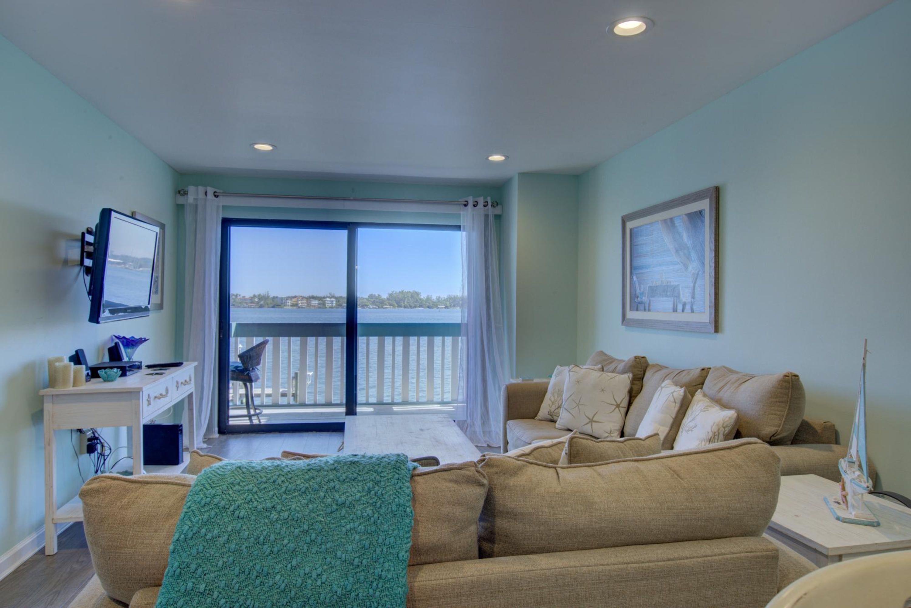 Une pièce comprenant un canapé, un bureau, une télévision et un balcon avec vue sur la mer.