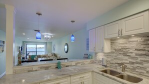 A modern kitchen with white cabinets, a stone backsplash, and a large island with a sink. - Anna Maria Island Retreat (Bradenton Beach)