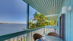 A balcony with a glass table and wicker chairs, overlooking a body of water and palm trees. - Anna Maria Island Retreat (Bradenton Beach)