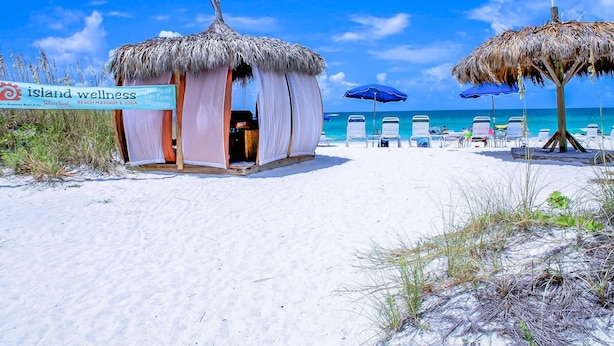 A beachside wellness center with a thatched-roof structure, beach chairs, and umbrellas. - Anna Maria Island Retreat (Bradenton Beach)