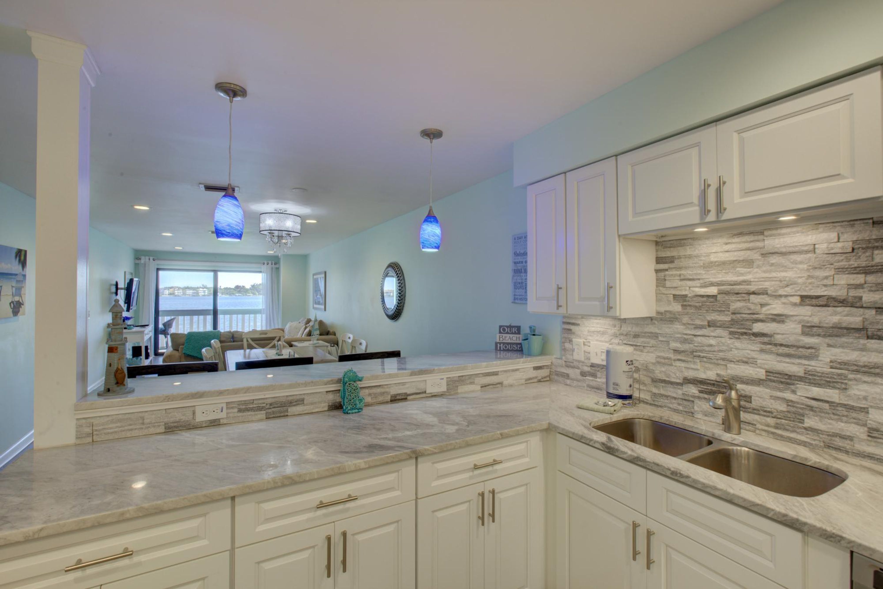 A modern kitchen with white cabinetry, a stone backsplash, and pendant lighting.