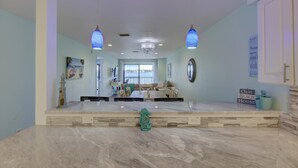 A spacious living area with a large marble countertop, two hanging blue pendant lights, a chandelier, and a view of the sea through large windows. - Anna Maria Island Retreat (Bradenton Beach)