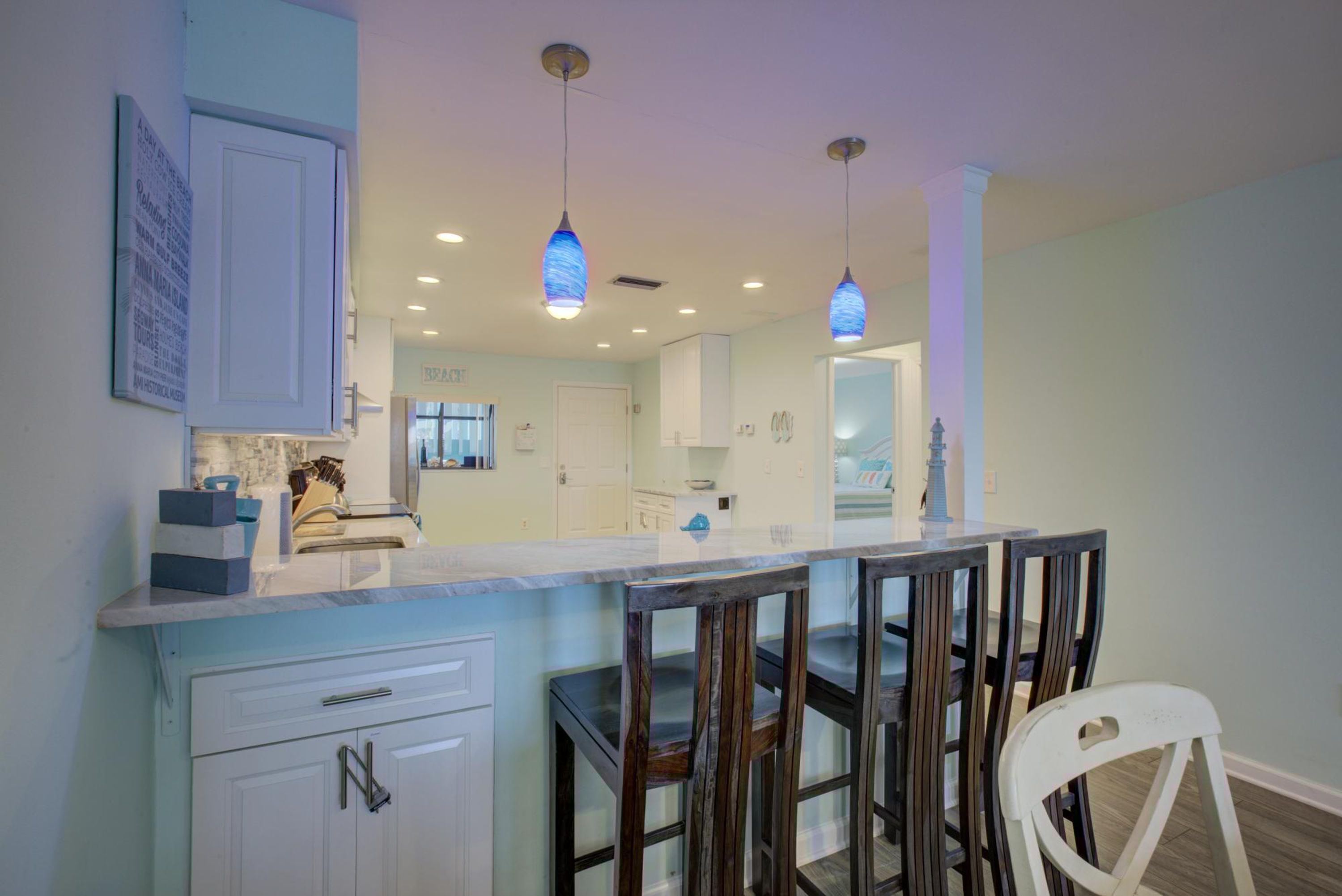A modern kitchen with a central island, pendant lighting, and a view into the dining area.