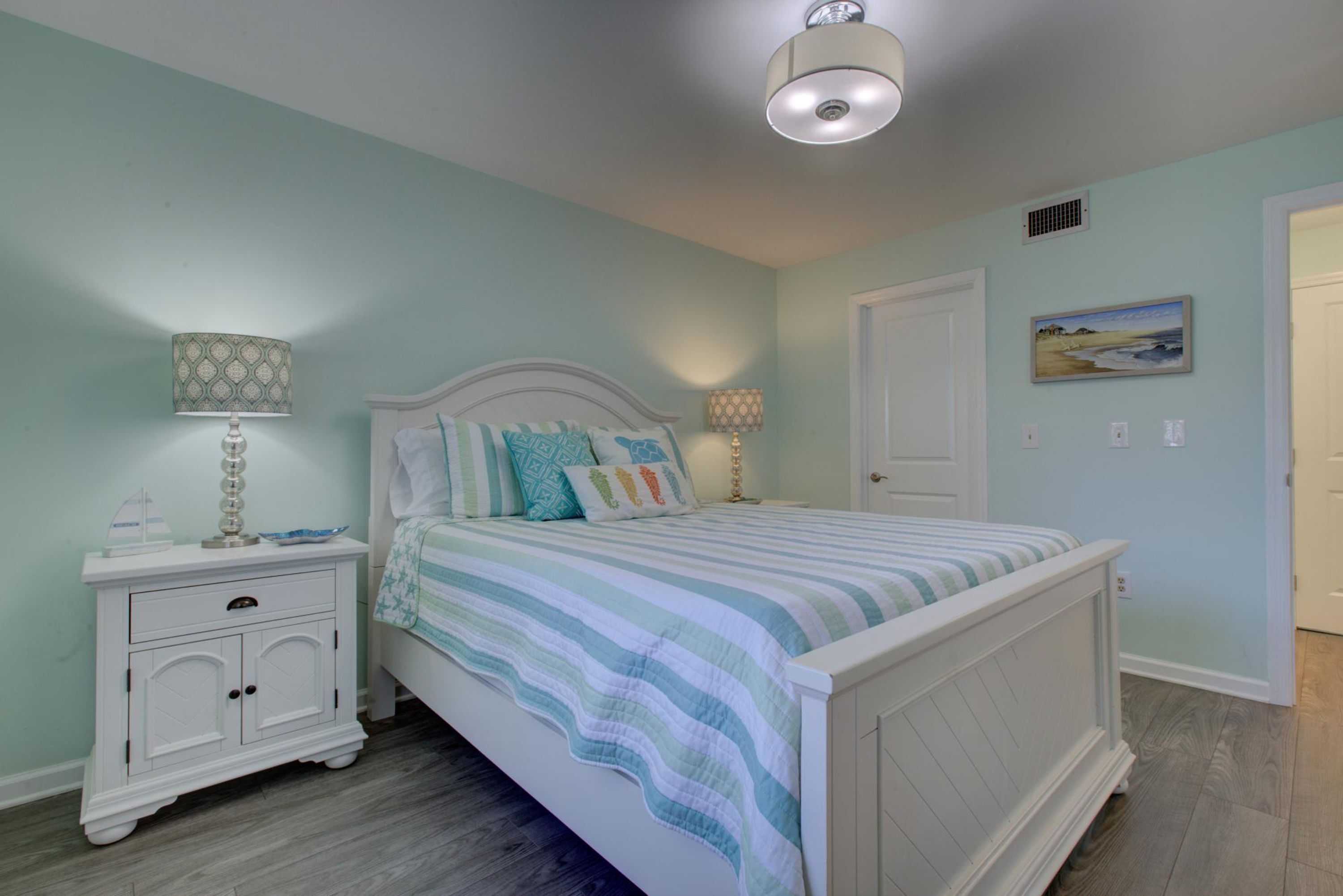 A bedroom with a bed, nightstands, a lamp, a door, and a painting on the wall.