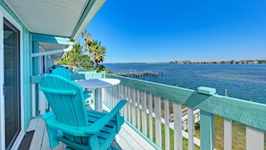 A balcony with turquoise chairs and a table overlooking a body of water with a dock. - Anna Maria Island Beach Palms 5B (Bradenton Beach)