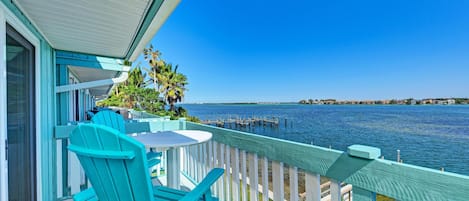 A balcony with turquoise chairs and a table overlooking a body of water with a dock.