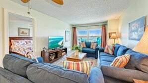 A living room with a sofa, a coffee table, a TV, and a view of the ocean. - Anna Maria Island Beach Palms 5B (Bradenton Beach)