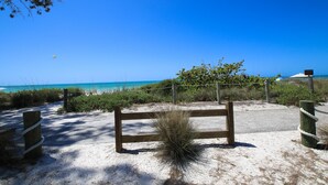 Ein Strandbereich mit Sand, einer Holzbank, einem Seilabfangnetz und einem Wegweiser.