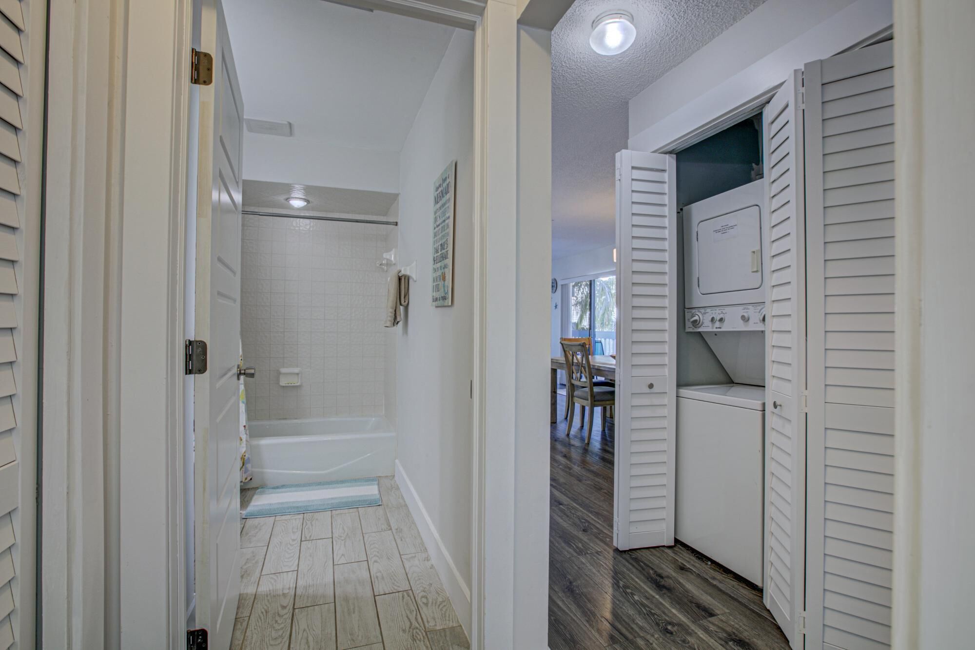 Un pasillo que da a un baño con ducha, un área de lavandería con lavadora y secadora, y un comedor visible a través de una puerta abierta.