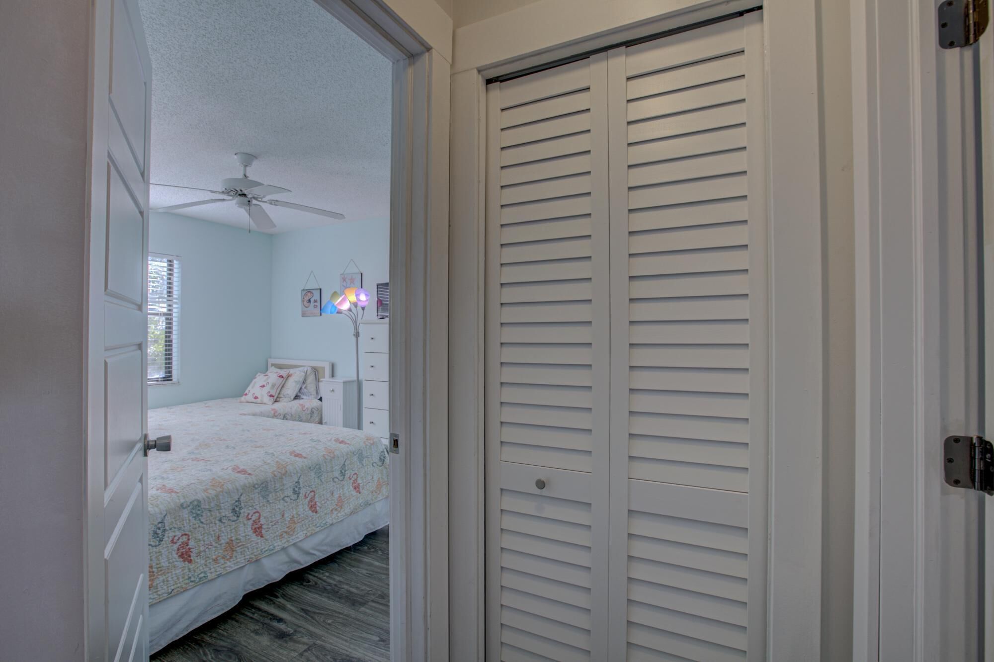 A bedroom with a bed, a ceiling fan, a bedside lamp, and a closet with louvered doors.