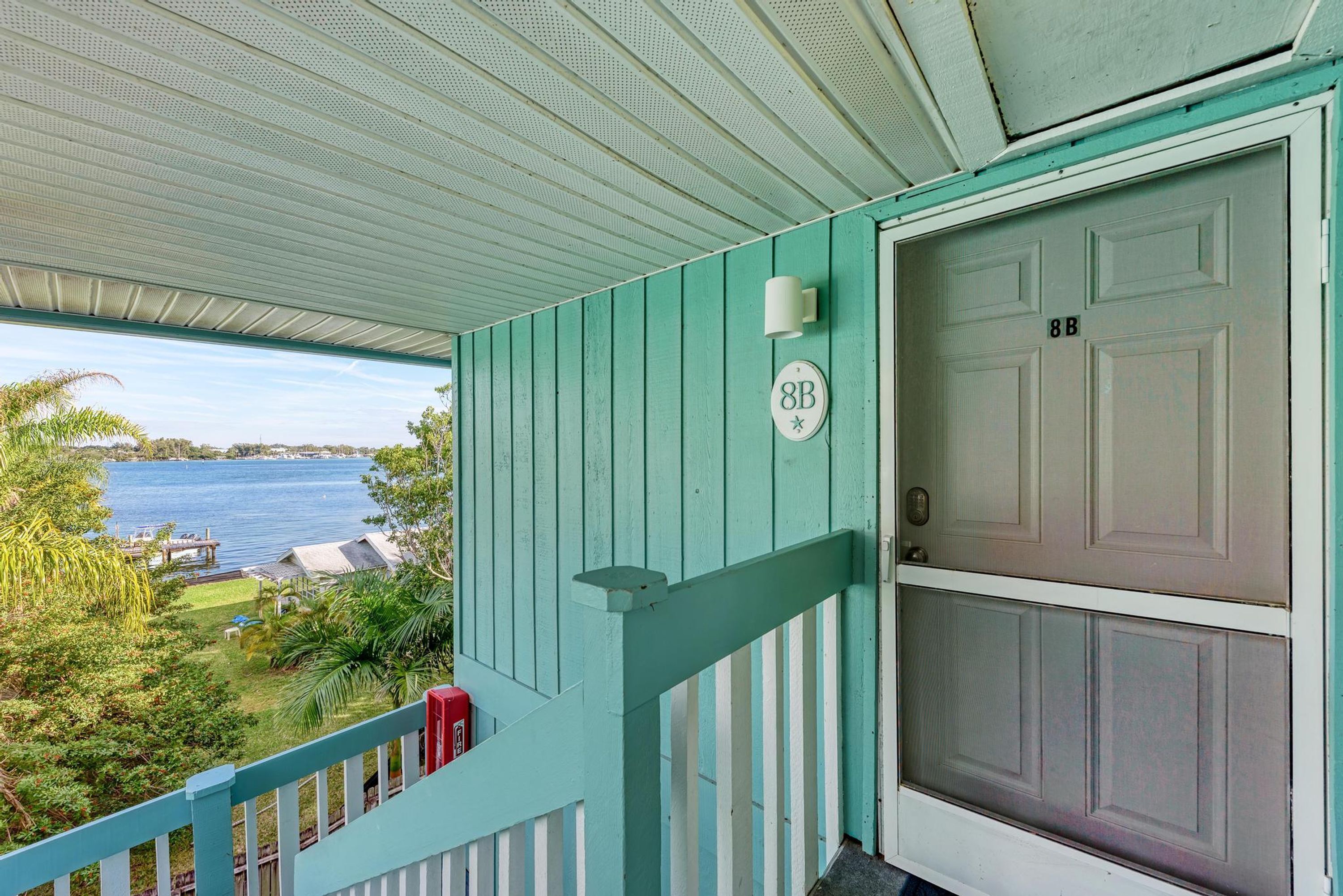 A turquoise porch with a white door marked "8B" and a view of a lake.