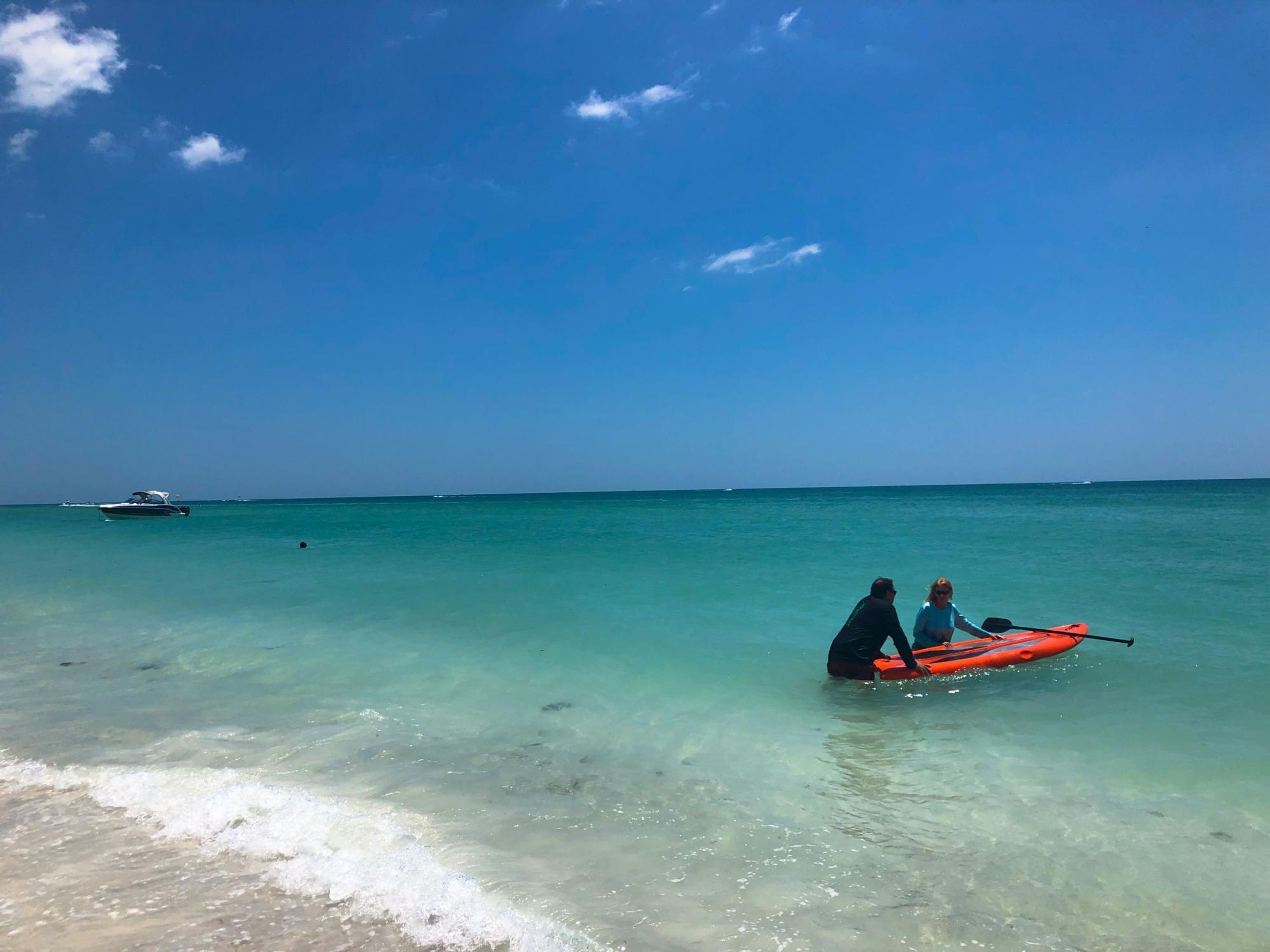 A clear blue sea with a boat in the distance and a kayak on the shore.