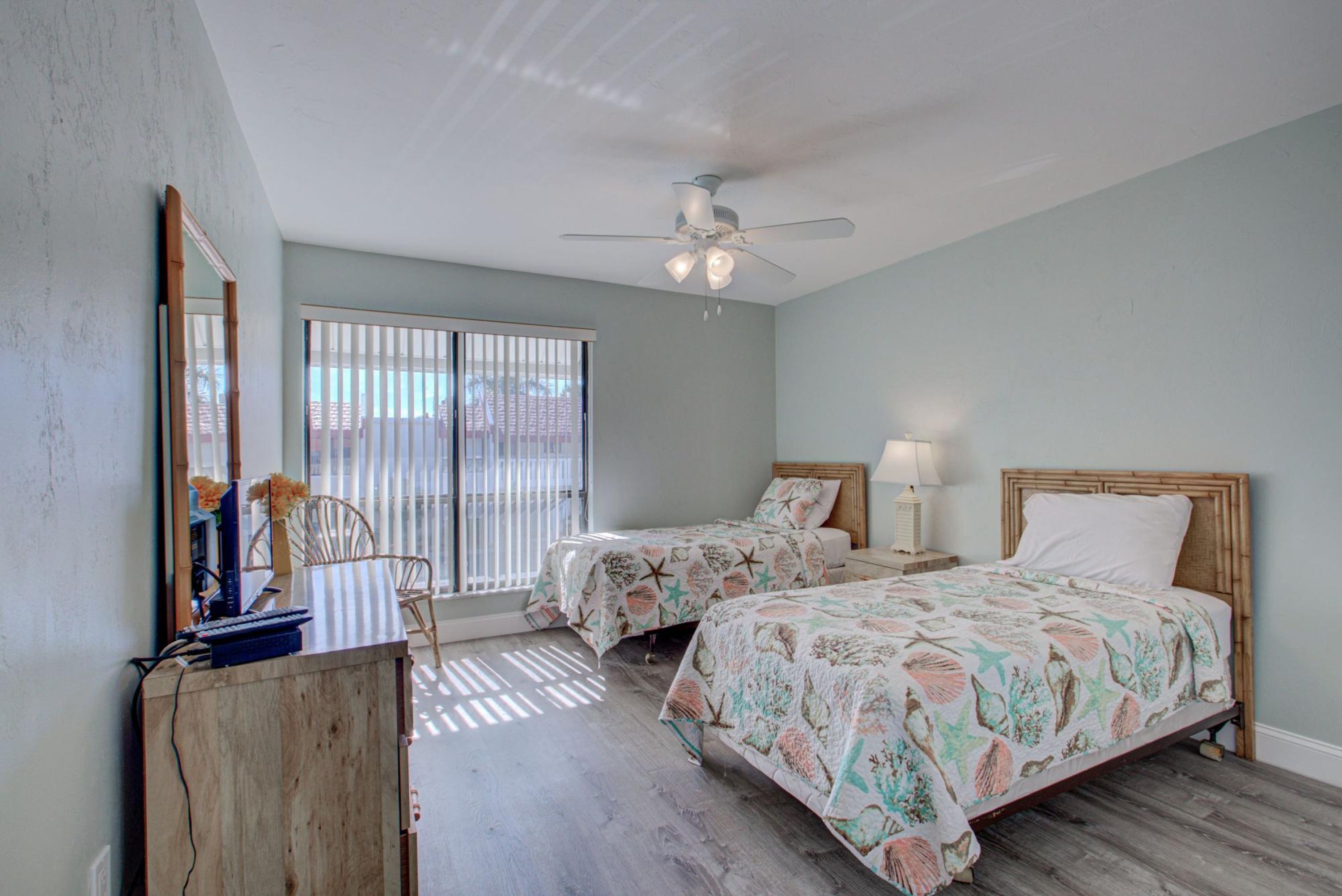 A bedroom with two beds, a desk, a chair, a ceiling fan, and a window with blinds.