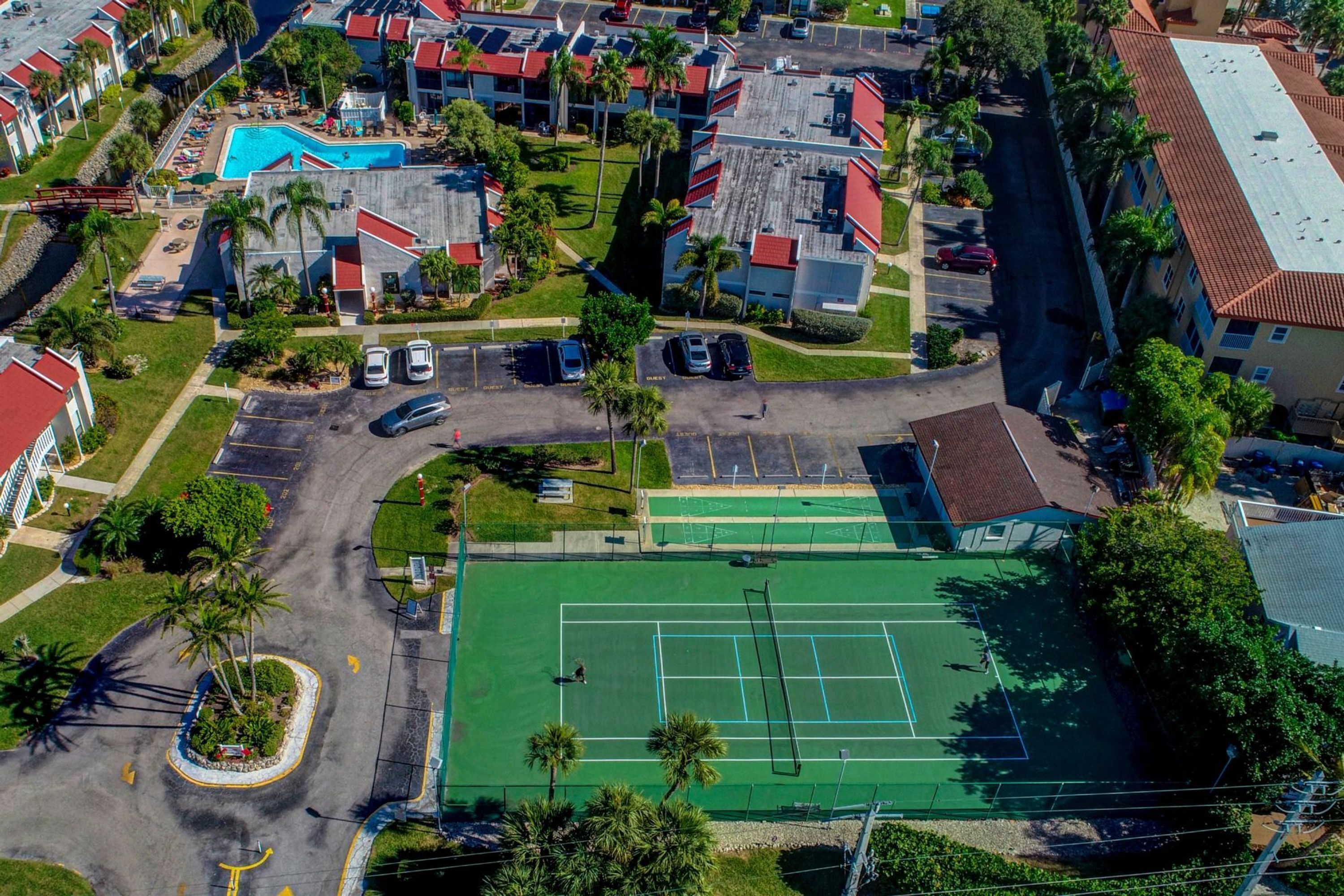 Vue aérienne d’un quartier résidentiel comprenant un court de tennis, une piscine et plusieurs bâtiments.