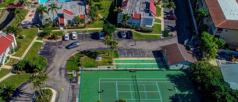Vue aérienne d’un quartier résidentiel comprenant un court de tennis, une piscine et plusieurs bâtiments.