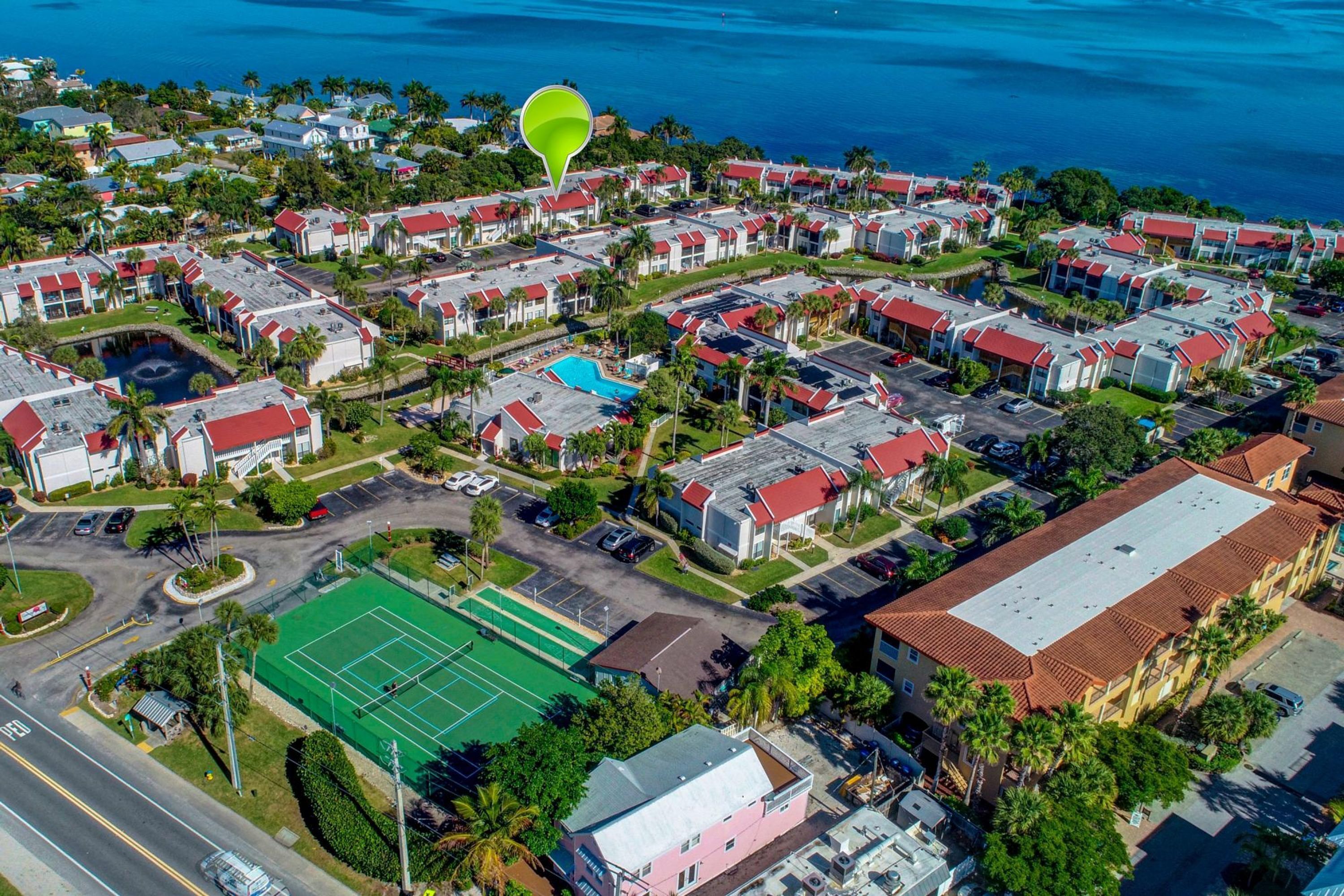 Vista aérea de una zona residencial con varios edificios, una cancha de tenis y una masa de agua al fondo.