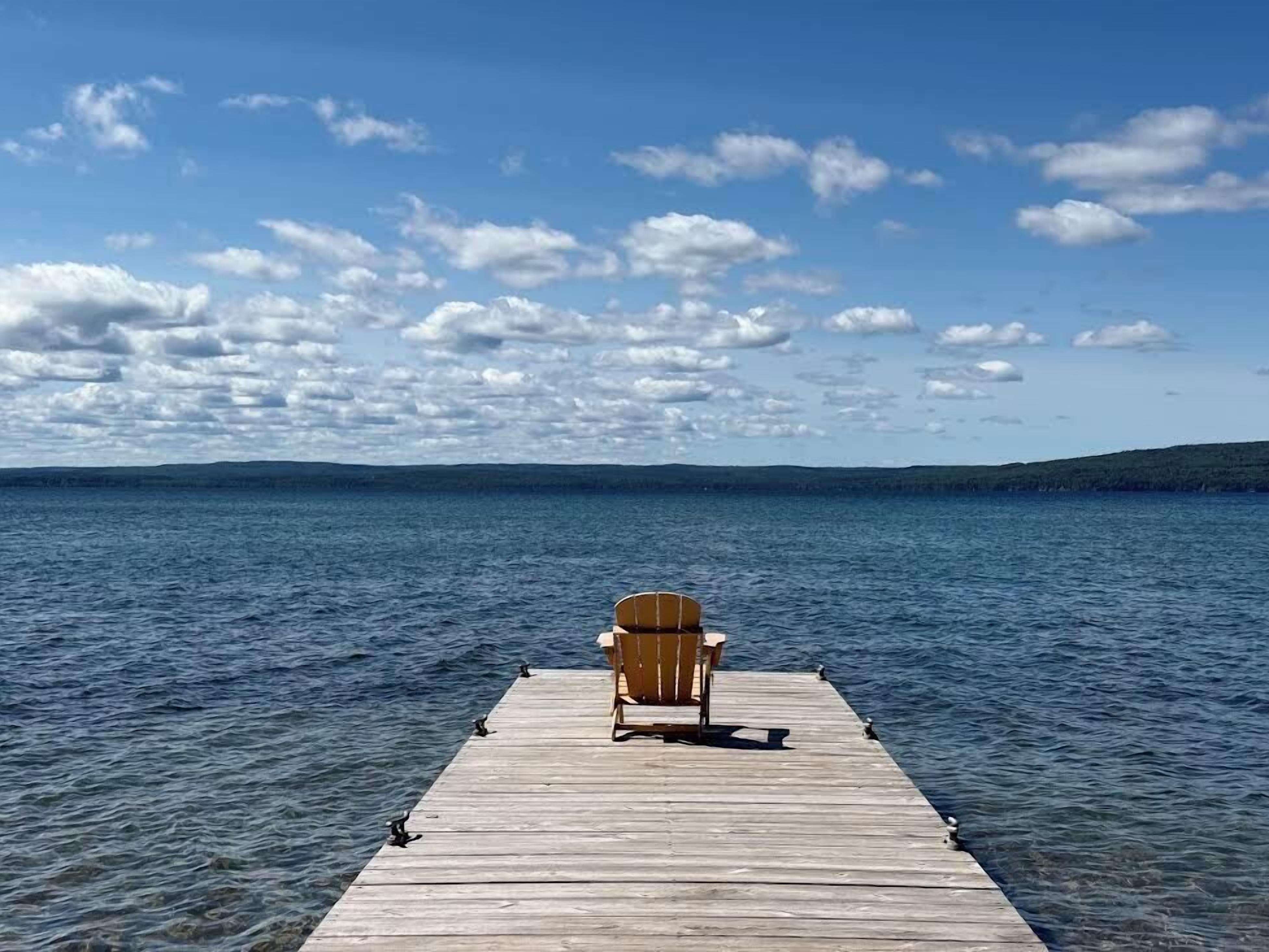 A wooden pier extending into a body of water with a single wooden chair at the end.