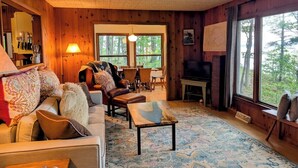 Un intérieur de chalet chaleureux avec une cheminée, des murs en bois, un canapé et un coin repas.
