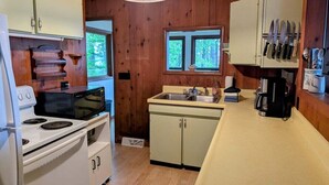 Une cuisine avec des murs en bois, un poêle blanc, un évier et des placards.
