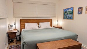 Une chambre à coucher comprenant un lit, des tables de chevet, une commode, un banc en bois, un tapis et des œuvres d’art murales.