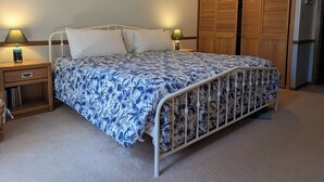 Un dormitorio con cama, mesitas de noche, aparador, armario de madera y un cuadro en la pared.