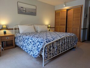 A bedroom with a bed, bedside tables, a nightstand, a wooden wardrobe, and a painting on the wall. - Slainte - Cottage located near Downtown La Pointe (La Pointe)