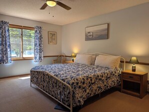 A bedroom with a bed, bedside tables, a window with curtains, a ceiling fan, and a painting on the wall. - Slainte - Cottage located near Downtown La Pointe (La Pointe)