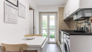 Cocina compacta con lavadora, comedor con mesa y sillas, y puerta que da a un balcón.