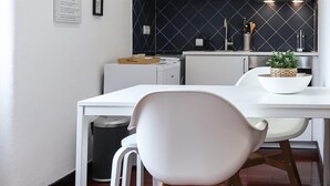 A modern kitchen with white cabinetry, a black backsplash, and a white dining area with a chair and table. - Belem Boutique IV by Homing (Lisbon)