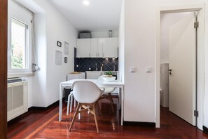 A compact kitchen with white cabinets, a black backsplash, and a dining area with a white table and chair. - Belem Boutique IV by Homing (Lisbon)