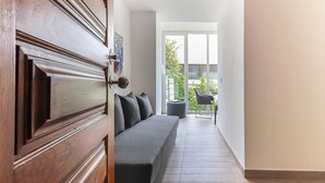 A modern interior with a wooden door, a grey sofa, and a view of an outdoor patio with a chair and table. - Belem Boutique VI by Homing (Lisbon)