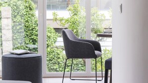 A modern room with a grey armchair, a small round ottoman, and a dining table. - Belem Boutique VI by Homing (Lisbon)