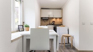 A narrow kitchen with white cabinets, a white countertop, and a small dining area with a chair and table.