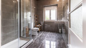 A modern bathroom with a glass shower enclosure, a toilet, a sink, and a window providing natural light. - Belem Boutique IX by Homing (Lisbon)