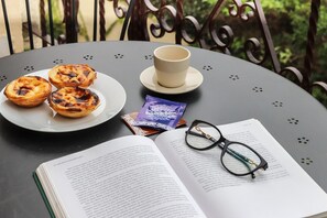 A table with a plate of pastries, a cup, a packet of tea, and an open book with glasses on it. - Belem Boutique VII by Homing (Lisbon)