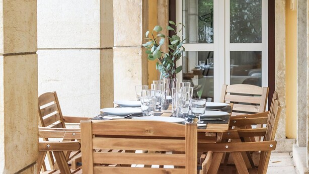 A wooden table set for dining with chairs, a vase with greenery, and a window in the background. - Belem Boutique II by Homing (Lisbon)