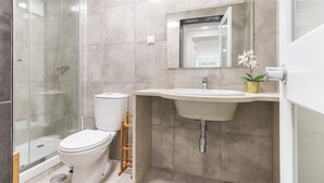 A modern bathroom with a glass-enclosed shower, a toilet, a sink with a mirror above it, and a small potted plant on the counter. - Belem Boutique II by Homing (Lisbon)