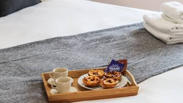 Uma bandeja com doces e xícaras sobre uma cama com cobertor cinzento.