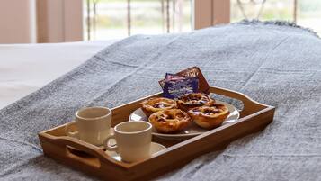 Uma bandeja com doces e duas chávenas sobre uma cama com um cobertor cinzento.